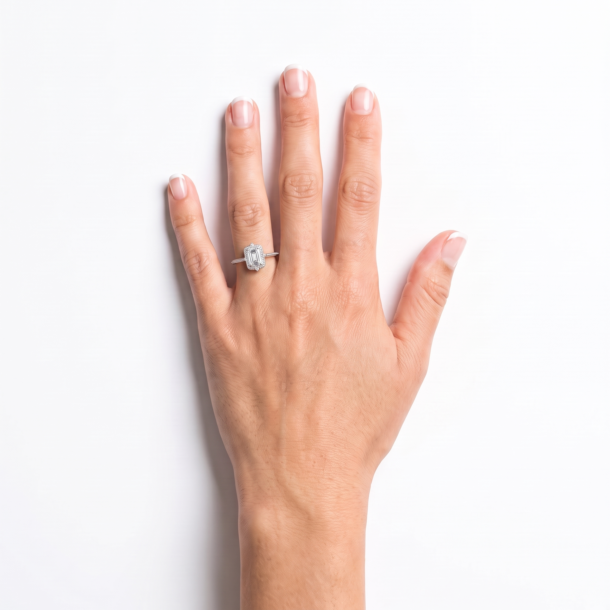 Emerald-cut halo engagement ring worn on the left hand, white gold shown