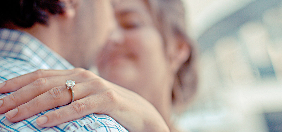 Diamond engagement ring on a woman's hand as she hugs her fiance