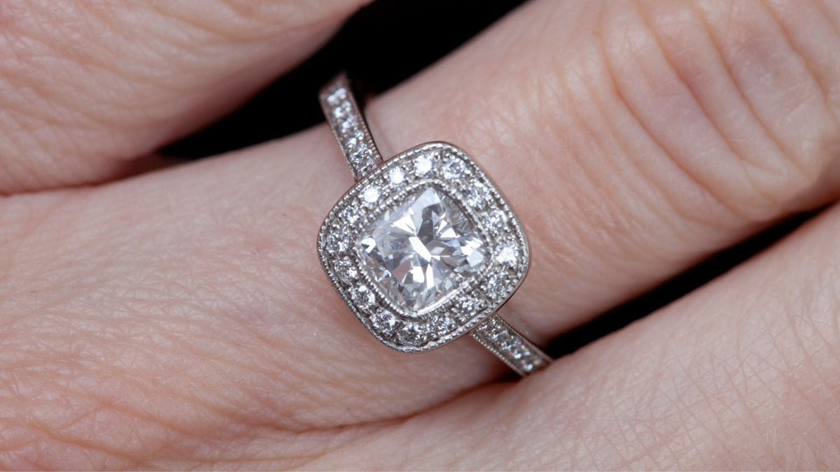 Cushion-cut halo engagement ring with milgrain edges on a woman's finger
