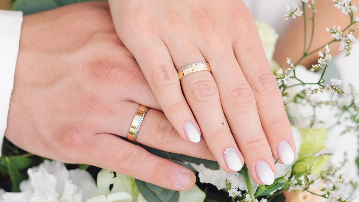 Couple's hands showing gold wedding bands, with white flowers