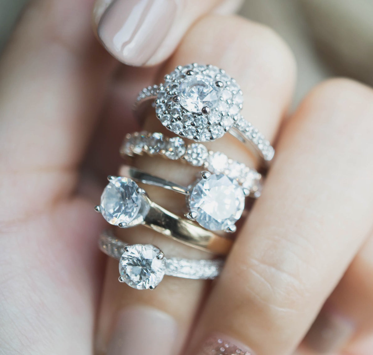 Stack of diamond engagement rings on a hand: a round halo, round solitaires and a diamond band